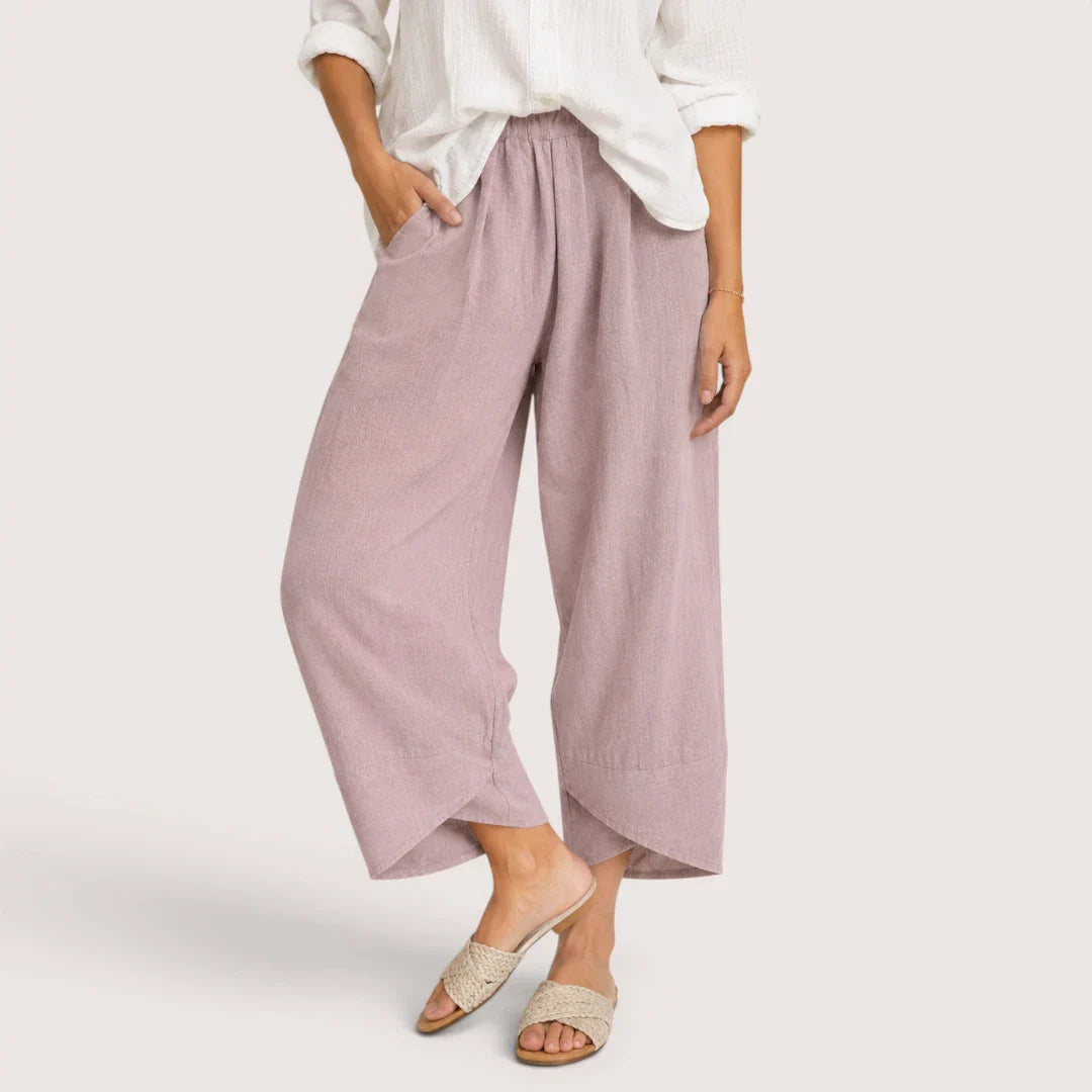 Person wearing light purple wide-leg pants and a white top on a plain background